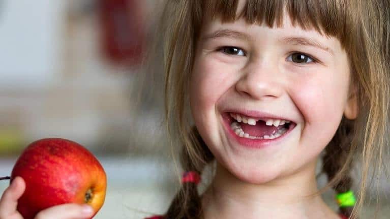 Child missing a tooth and holding an apple